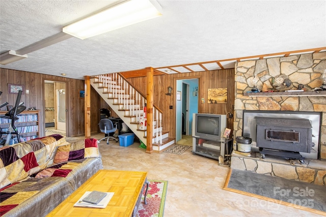 carpeted living room with wooden walls, a textured ceiling, and a wood stove