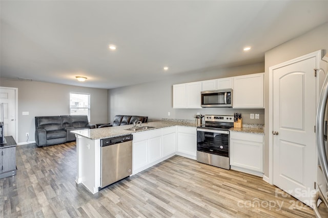 kitchen featuring stainless steel appliances, kitchen peninsula, sink, and white cabinets