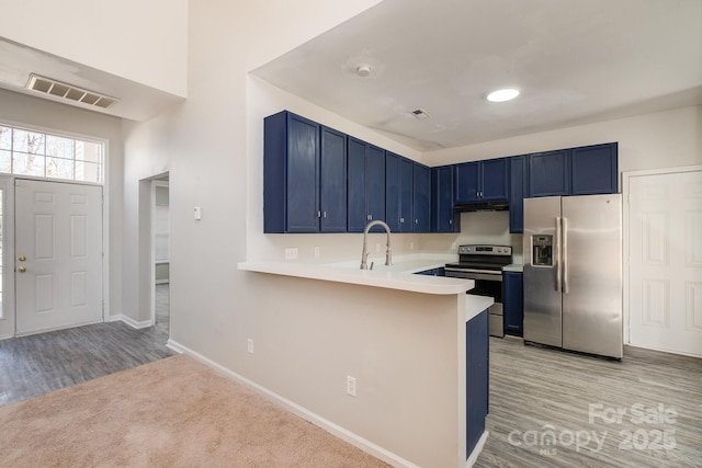 kitchen with stainless steel appliances, blue cabinets, light hardwood / wood-style floors, and kitchen peninsula