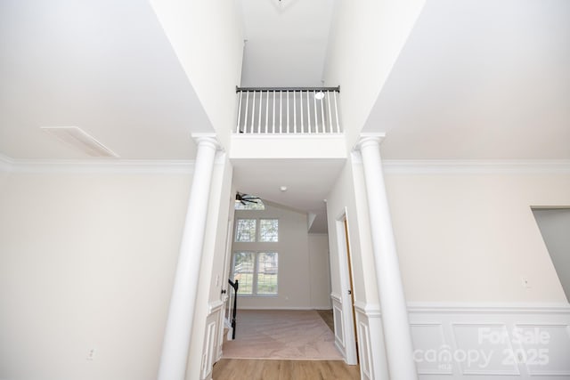 stairs featuring decorative columns, crown molding, wood-type flooring, and a high ceiling