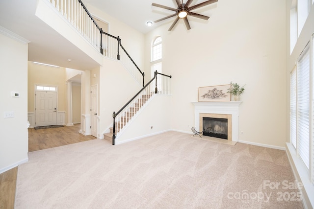 unfurnished living room featuring ceiling fan, a towering ceiling, light carpet, and a fireplace