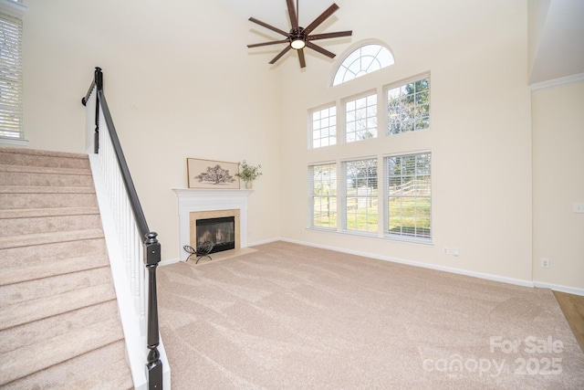 unfurnished living room with light carpet, ceiling fan, a towering ceiling, and a healthy amount of sunlight