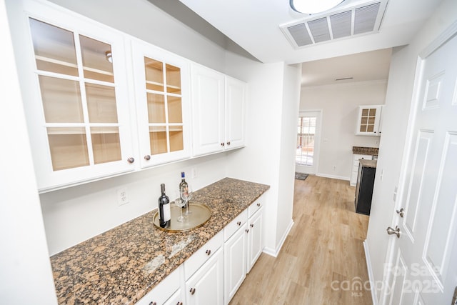 bar with white cabinetry, ornamental molding, dark stone countertops, and light wood-type flooring