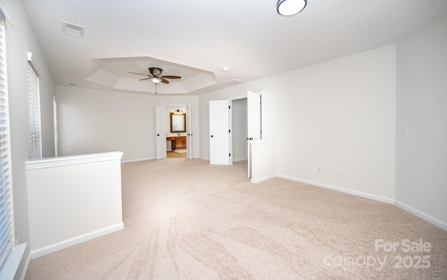 unfurnished room featuring light carpet, a tray ceiling, and ceiling fan