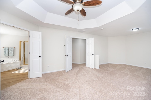 unfurnished bedroom with light colored carpet, a raised ceiling, and ensuite bath