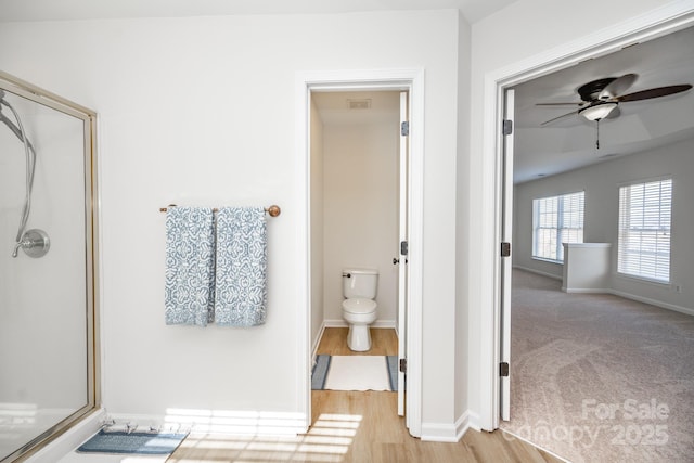 bathroom featuring ceiling fan, hardwood / wood-style flooring, a shower with shower door, and toilet