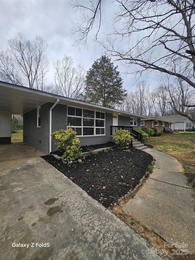 view of front of home featuring concrete driveway, brick siding, crawl space, and an attached carport