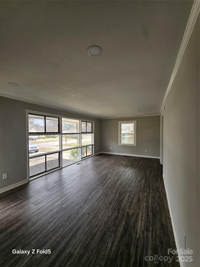 empty room featuring dark wood-style floors, ornamental molding, and baseboards