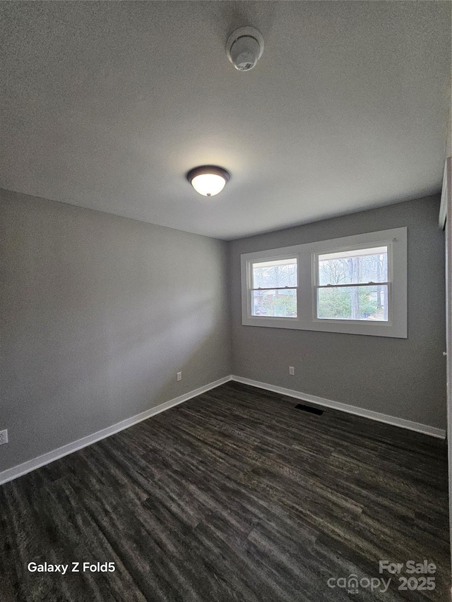 spare room featuring visible vents, dark wood finished floors, and baseboards