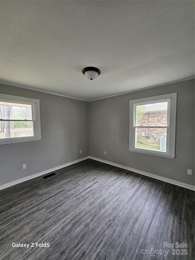 empty room featuring baseboards, crown molding, visible vents, and dark wood-style flooring