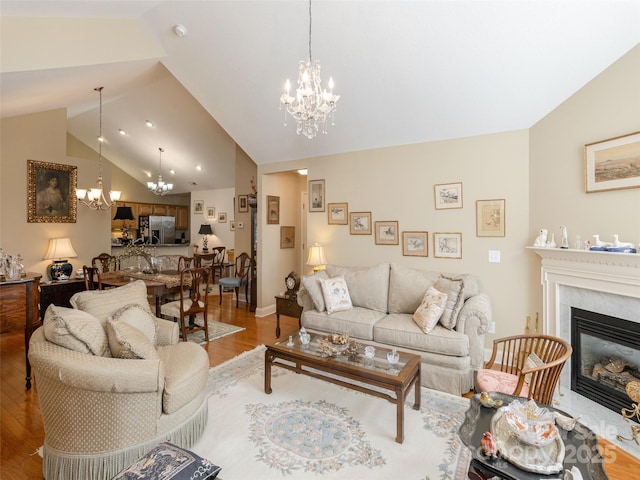 living room with hardwood / wood-style flooring, a high end fireplace, vaulted ceiling, and a notable chandelier