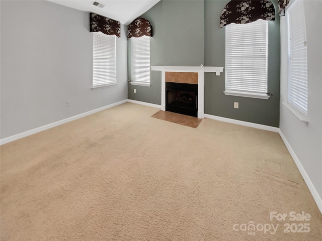 unfurnished living room with a tile fireplace, lofted ceiling, and light colored carpet