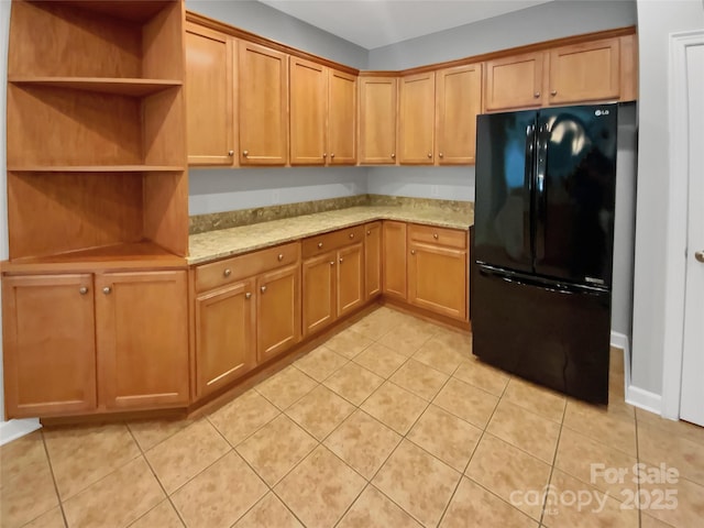 kitchen featuring light tile patterned flooring, light stone countertops, and black fridge