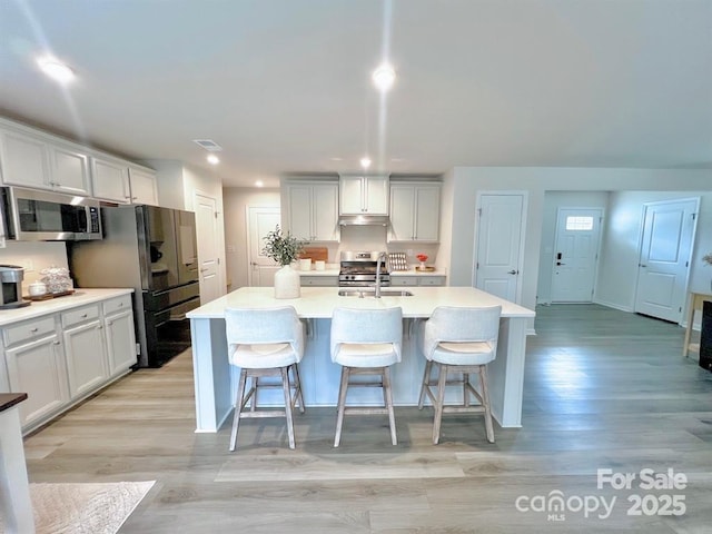 kitchen featuring stainless steel appliances, a kitchen island with sink, and a kitchen breakfast bar