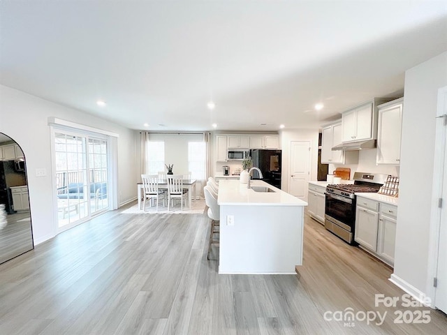 kitchen with appliances with stainless steel finishes, a breakfast bar, white cabinetry, sink, and a center island with sink