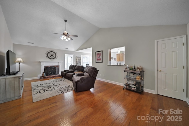 living room with baseboards, a ceiling fan, lofted ceiling, wood finished floors, and a brick fireplace