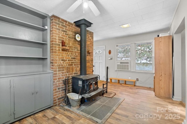 living room featuring built in shelves, light hardwood / wood-style flooring, ceiling fan, and a wood stove