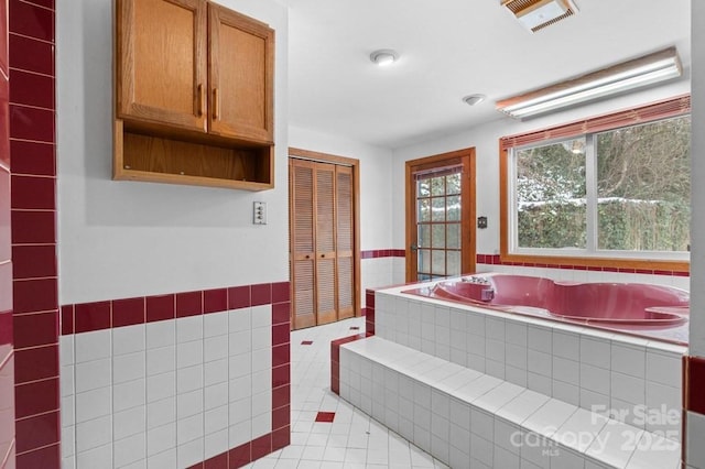 bathroom with a relaxing tiled tub, tile patterned floors, and tile walls