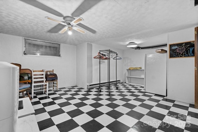 basement with ceiling fan, a textured ceiling, white fridge, and a baseboard heating unit