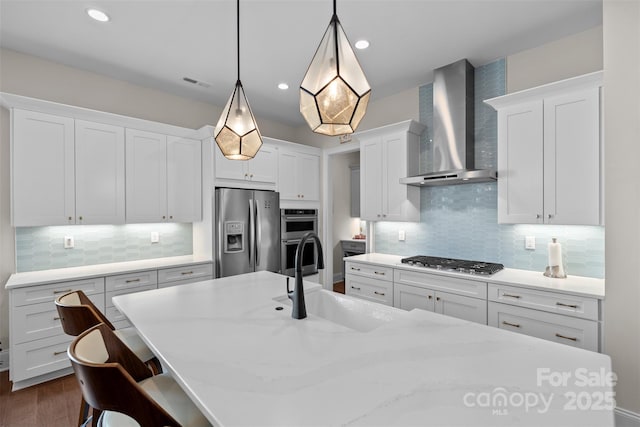 kitchen featuring pendant lighting, sink, appliances with stainless steel finishes, white cabinets, and wall chimney exhaust hood