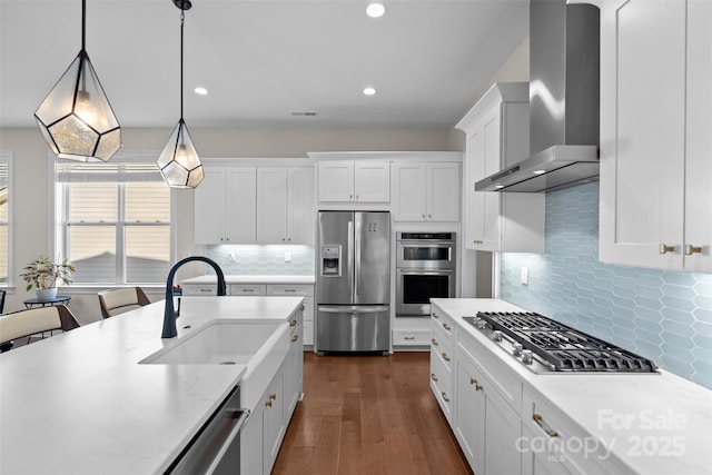 kitchen featuring wall chimney exhaust hood, sink, white cabinetry, hanging light fixtures, and appliances with stainless steel finishes