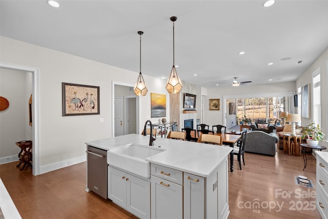 kitchen featuring hardwood / wood-style floors, pendant lighting, white cabinetry, sink, and a center island with sink