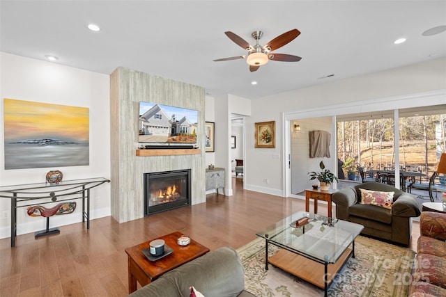 living room with hardwood / wood-style flooring, a large fireplace, and ceiling fan