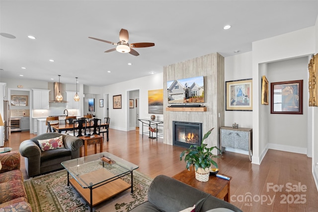 living room with ceiling fan, a large fireplace, sink, and hardwood / wood-style floors