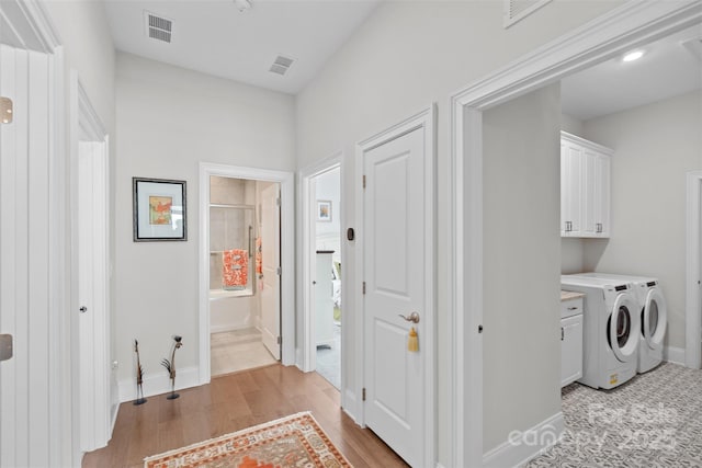 laundry room featuring separate washer and dryer, light hardwood / wood-style flooring, and cabinets