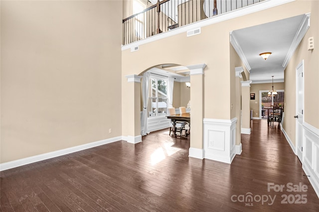 foyer entrance featuring crown molding, a towering ceiling, dark hardwood / wood-style floors, and ornate columns