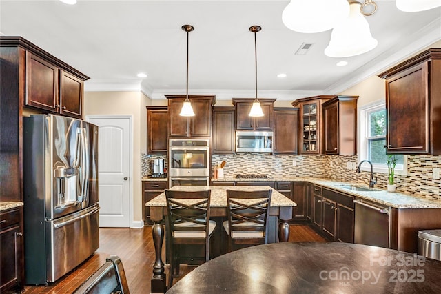 kitchen featuring pendant lighting, sink, stainless steel appliances, light stone countertops, and a kitchen island