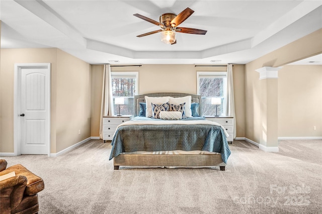 carpeted bedroom with a raised ceiling, ceiling fan, and decorative columns