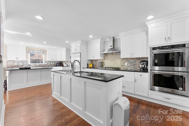 kitchen featuring wall chimney exhaust hood, white cabinetry, appliances with stainless steel finishes, dark hardwood / wood-style floors, and a kitchen island