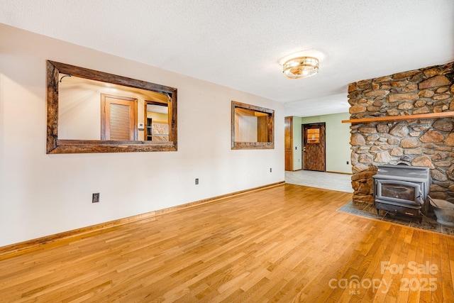 unfurnished living room featuring a wood stove, a textured ceiling, baseboards, and wood finished floors