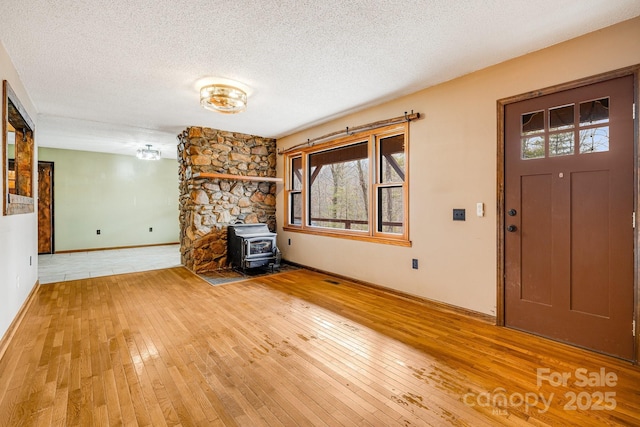 unfurnished living room with wood-type flooring, a textured ceiling, and a wood stove