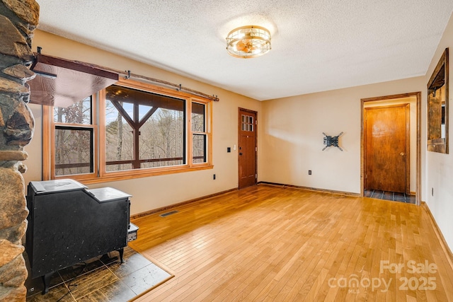 interior space featuring visible vents, a wood stove, a textured ceiling, and hardwood / wood-style flooring