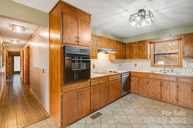 kitchen featuring brown cabinets, under cabinet range hood, light countertops, black appliances, and a sink