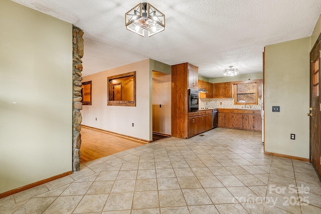 kitchen with a textured ceiling, black oven, light tile patterned floors, and brown cabinetry