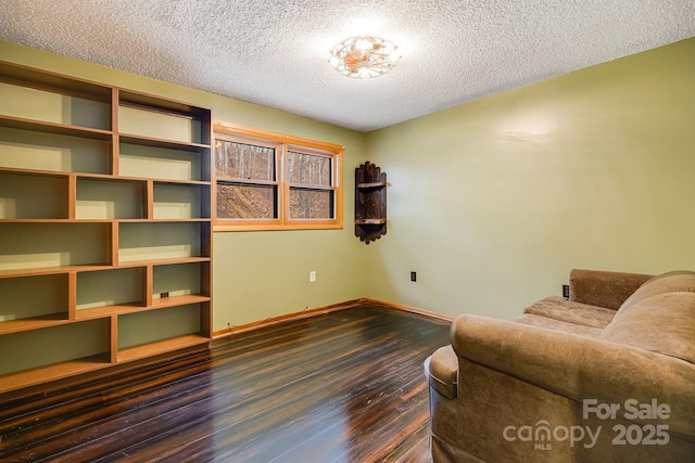 living area with a textured ceiling, dark wood-type flooring, and baseboards