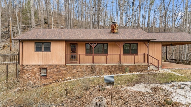 view of front facade with a chimney, an attached carport, roof with shingles, covered porch, and brick siding