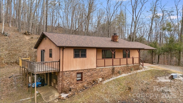 view of property exterior with covered porch, a shingled roof, brick siding, dirt driveway, and a chimney