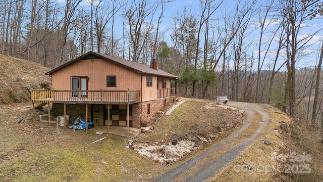 view of side of home with driveway, a chimney, and a wooden deck