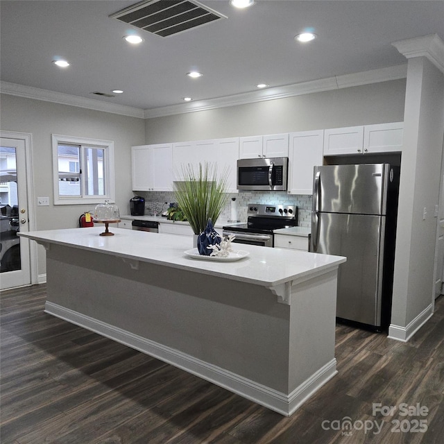 kitchen featuring dark wood-type flooring, a center island, ornamental molding, appliances with stainless steel finishes, and white cabinets