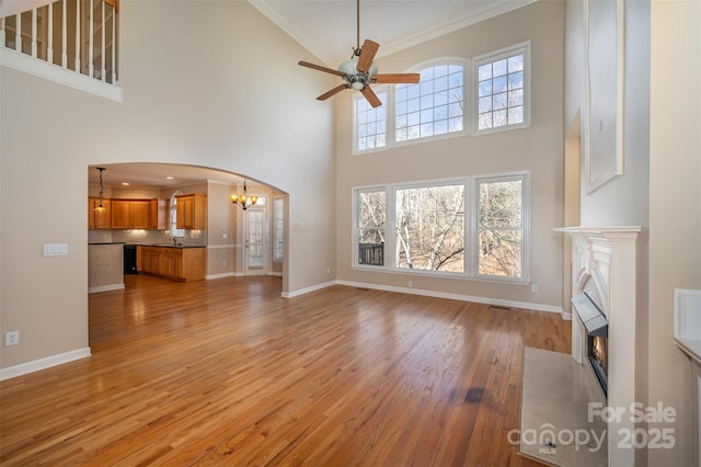 unfurnished living room with sink, ceiling fan with notable chandelier, ornamental molding, and light wood-type flooring