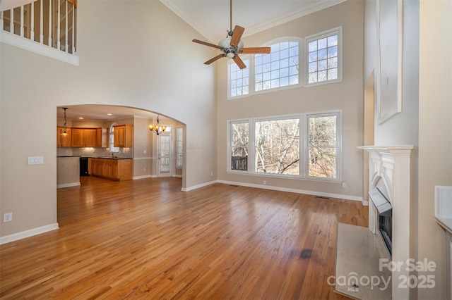 unfurnished living room with ornamental molding, sink, ceiling fan with notable chandelier, and light hardwood / wood-style flooring