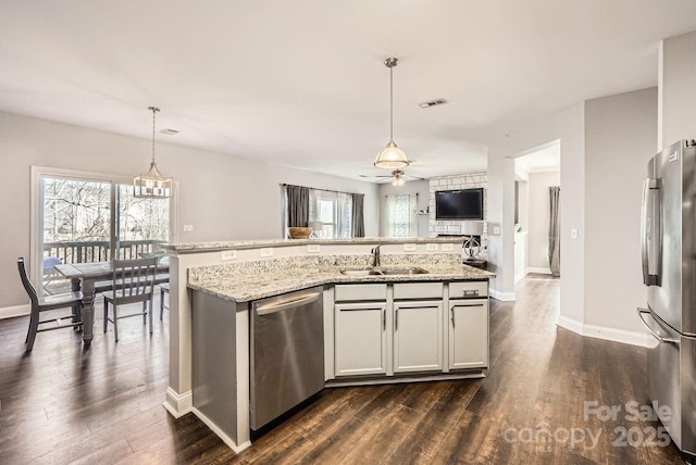 kitchen with sink, appliances with stainless steel finishes, dark hardwood / wood-style floors, light stone countertops, and decorative light fixtures