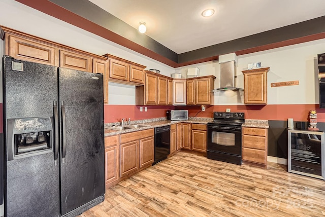 kitchen with wall chimney exhaust hood, sink, light hardwood / wood-style flooring, beverage cooler, and black appliances