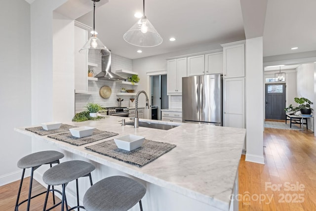 kitchen with wall chimney exhaust hood, sink, hanging light fixtures, stainless steel appliances, and white cabinets