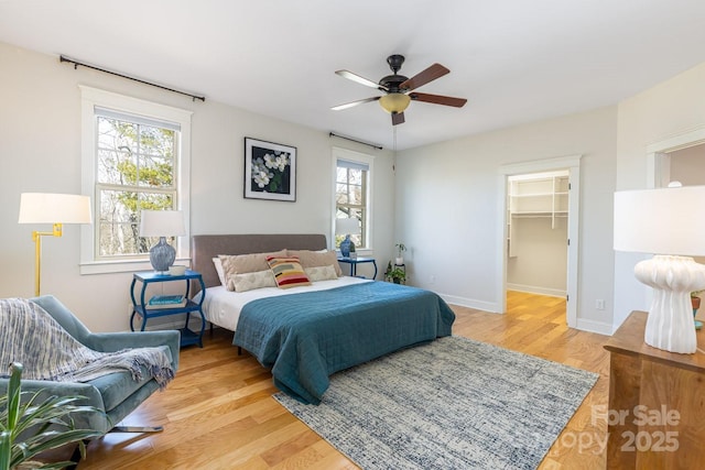 bedroom with ceiling fan, a spacious closet, a closet, and light wood-type flooring