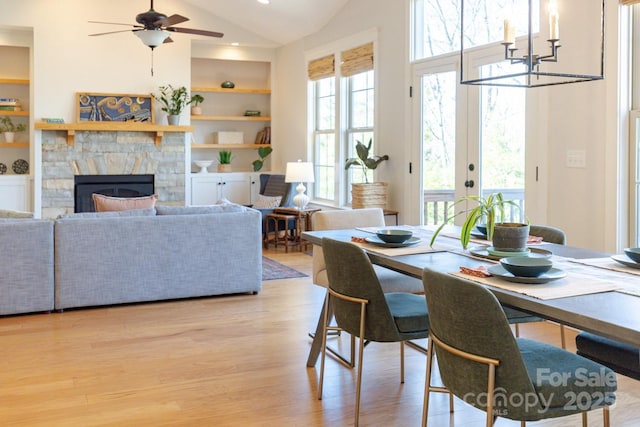 dining area with built in features, high vaulted ceiling, a fireplace, light hardwood / wood-style floors, and french doors